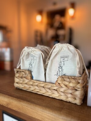 A woven basket containing two drawstring bags labeled "Hangover Kit" on a wooden surface. - Pupa Alacati Butik Otel (Cesme)