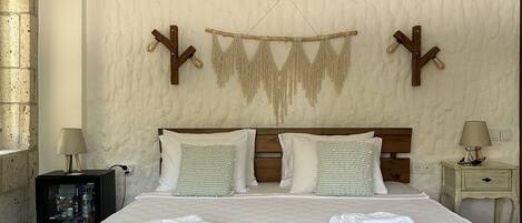 A bedroom with a large wooden bed, two bedside tables, a wall-mounted air conditioner, and a hanging macrame decoration.