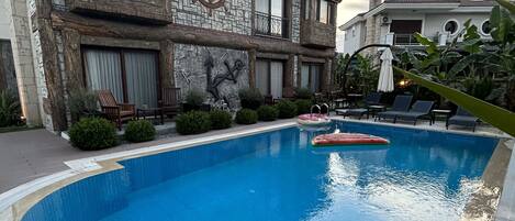 Une piscine dotée d’une façade en pierre et d’une grande fresque représentant une ancre, entourée de chaises longues et d’un jardin bien entretenu.