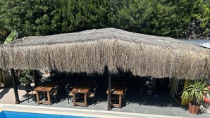 Una piscina con copertura in paglia e zona relax in legno.