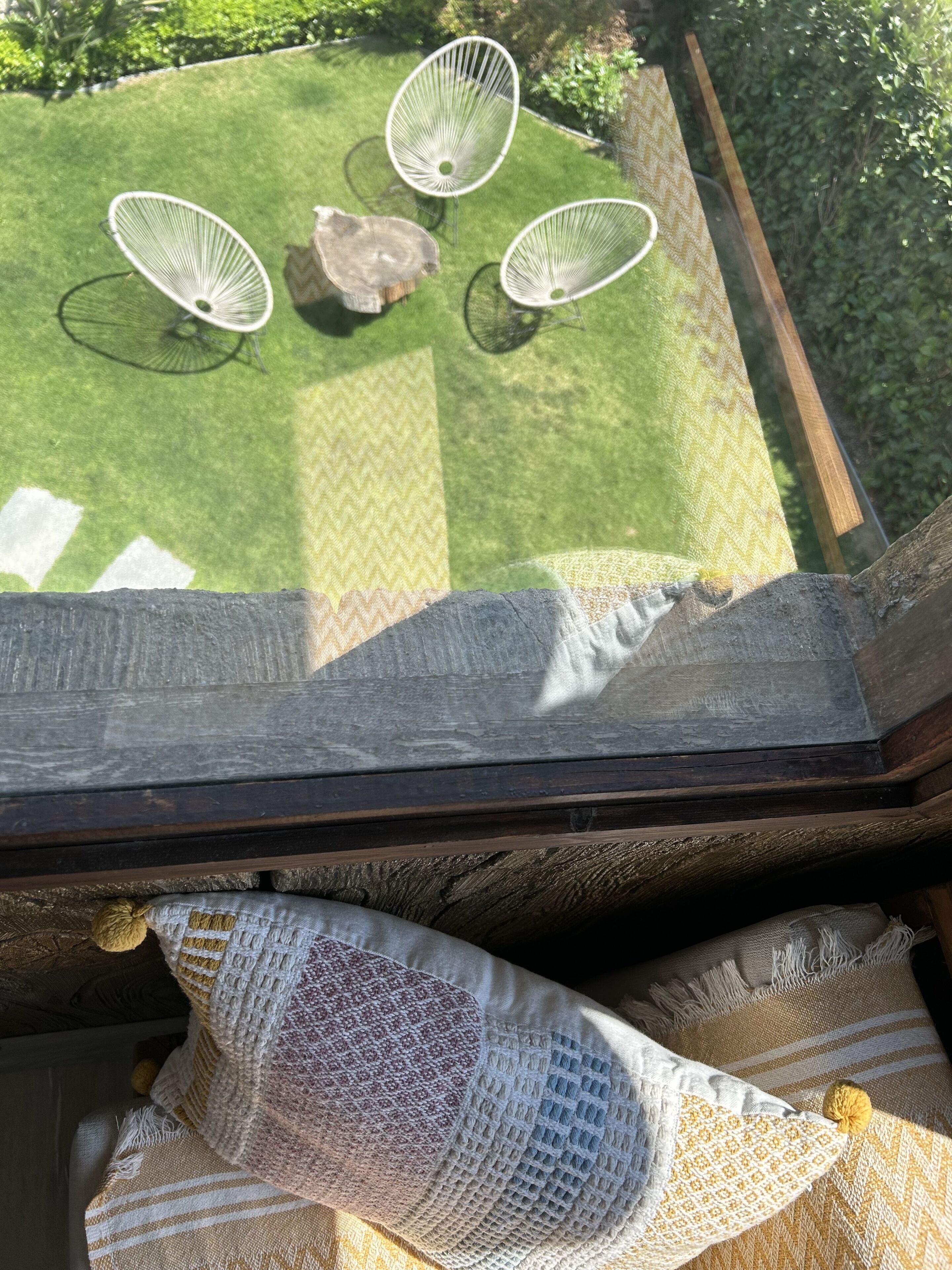 A view from a balcony overlooking a garden with a wooden table and four white wire chairs.