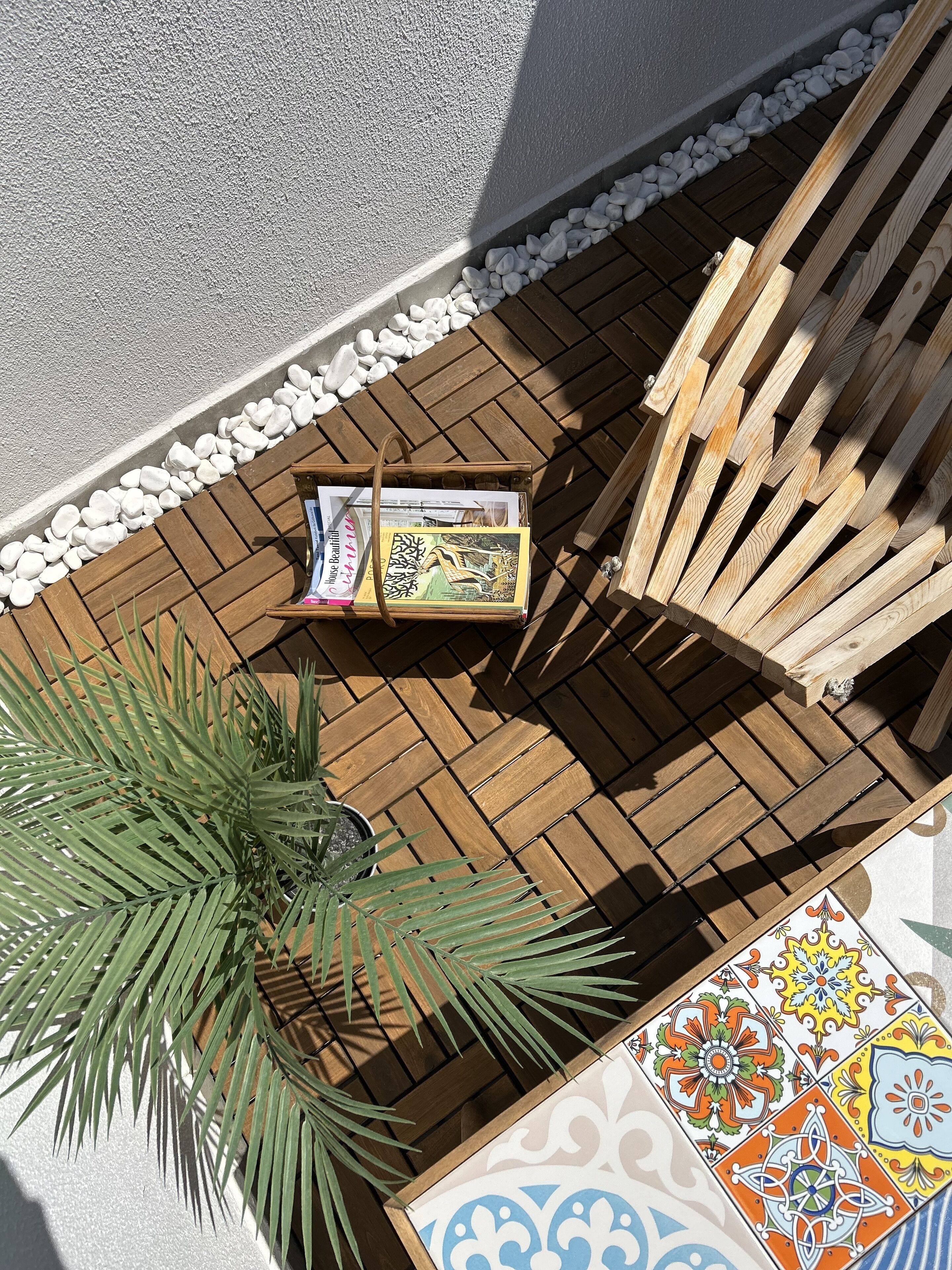 A wooden deck with a palm plant, a wooden bench, and a tiled area with a colorful pattern.