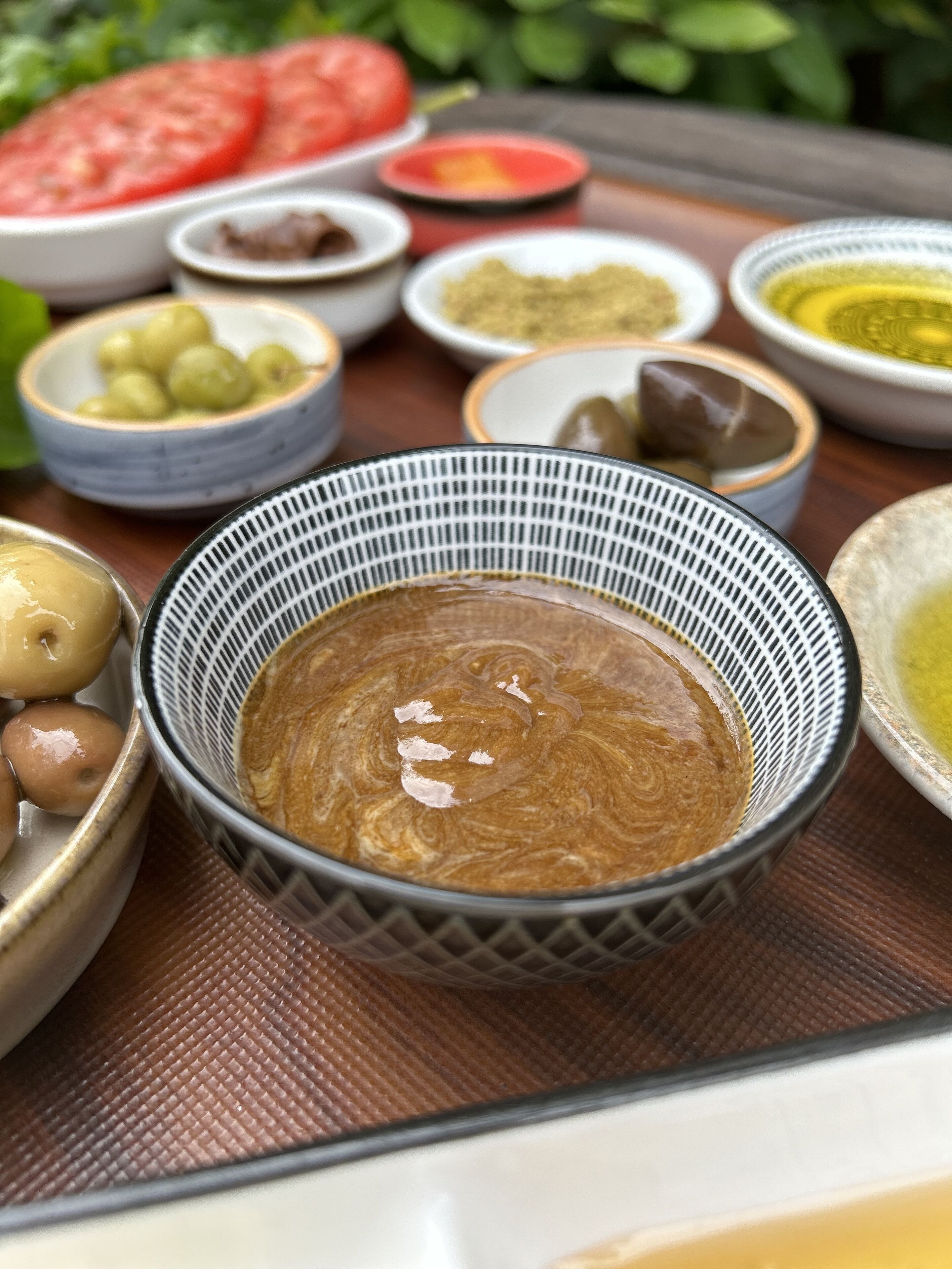Uma mesa com diversos alimentos, incluindo azeitonas, tomates e recipientes com molhos.