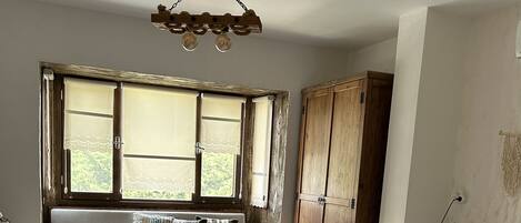 A bedroom with a wooden bed, a bench with cushions, a wooden wardrobe, and a window with curtains.