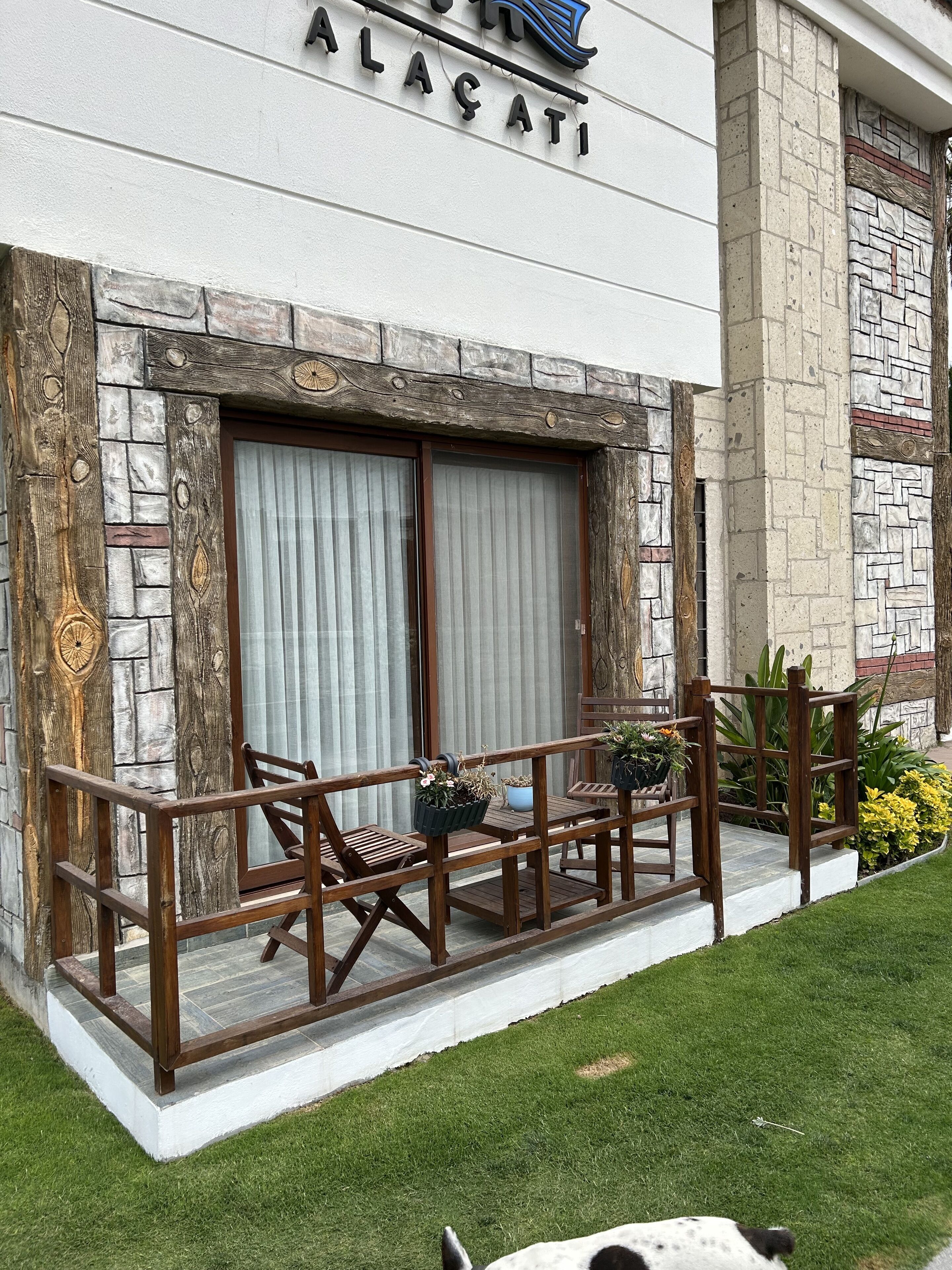 A building with a stone facade, a wooden balcony with seating, and a sign reading "ALACATI".