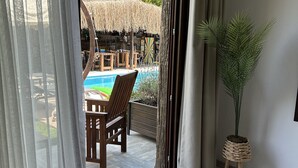 Una stanza con un'ampia porta-finestra scorrevole che si apre su una zona piscina, un pontile di legno e una pianta in vaso.