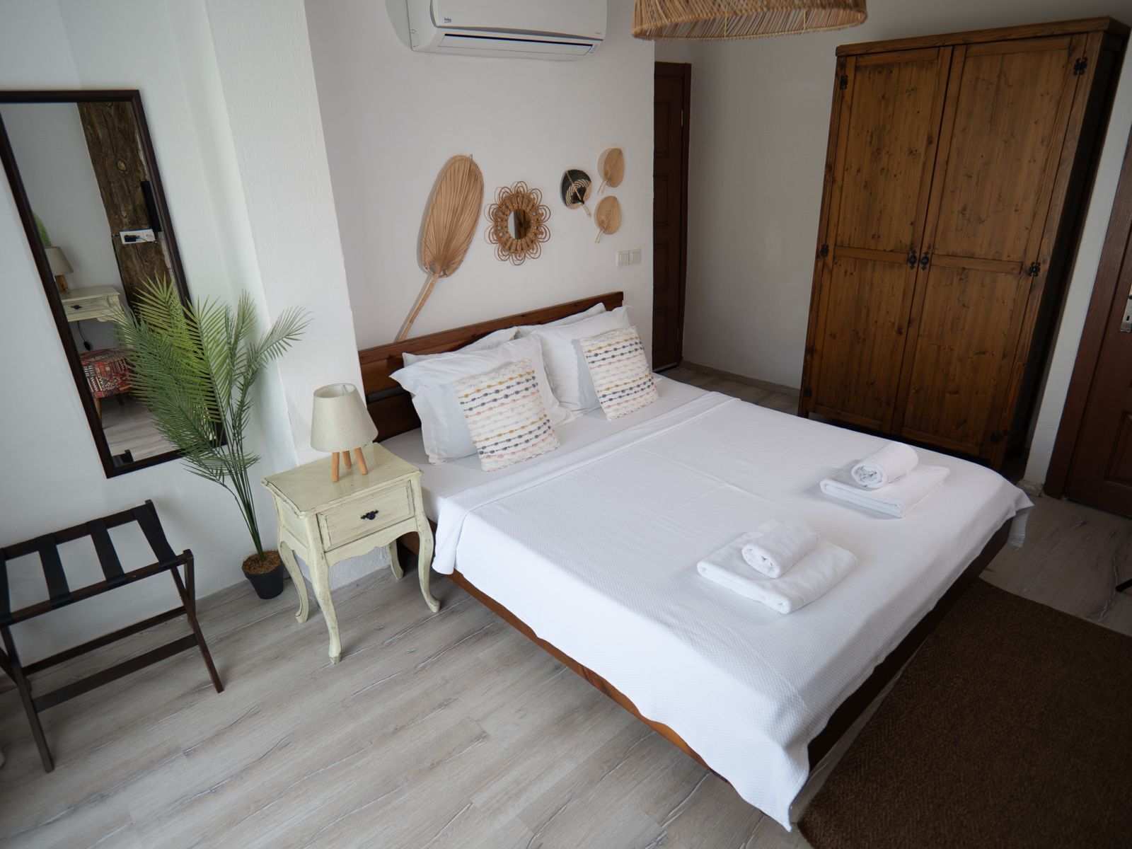 A bedroom with a bed, bedside table, lamp, potted plant, wooden bench, and a wardrobe.