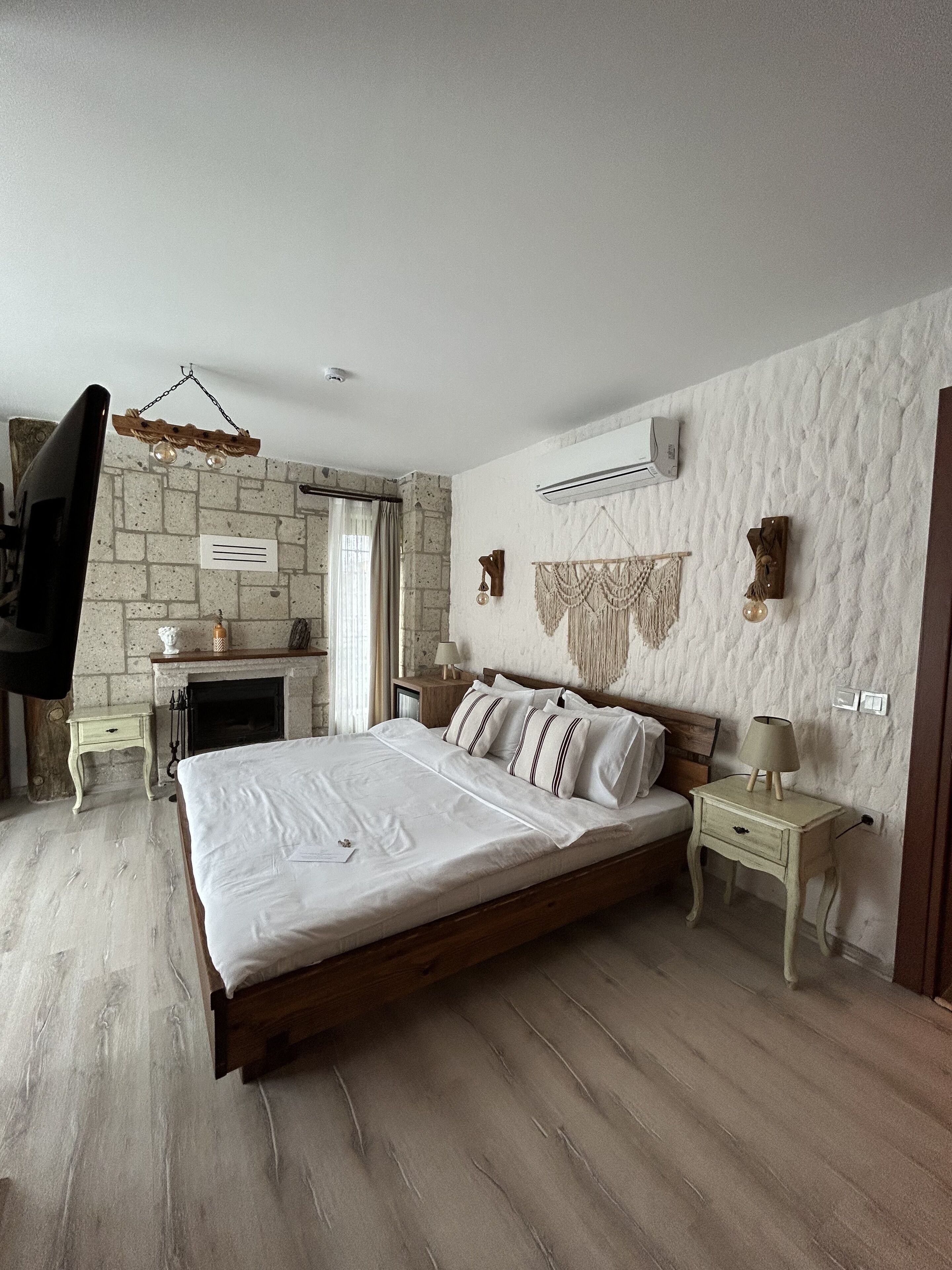 Een slaapkamer met een bed, nachtkastjes, een klein tafeltje, een hanglamp, een open haard en een stenen muur.