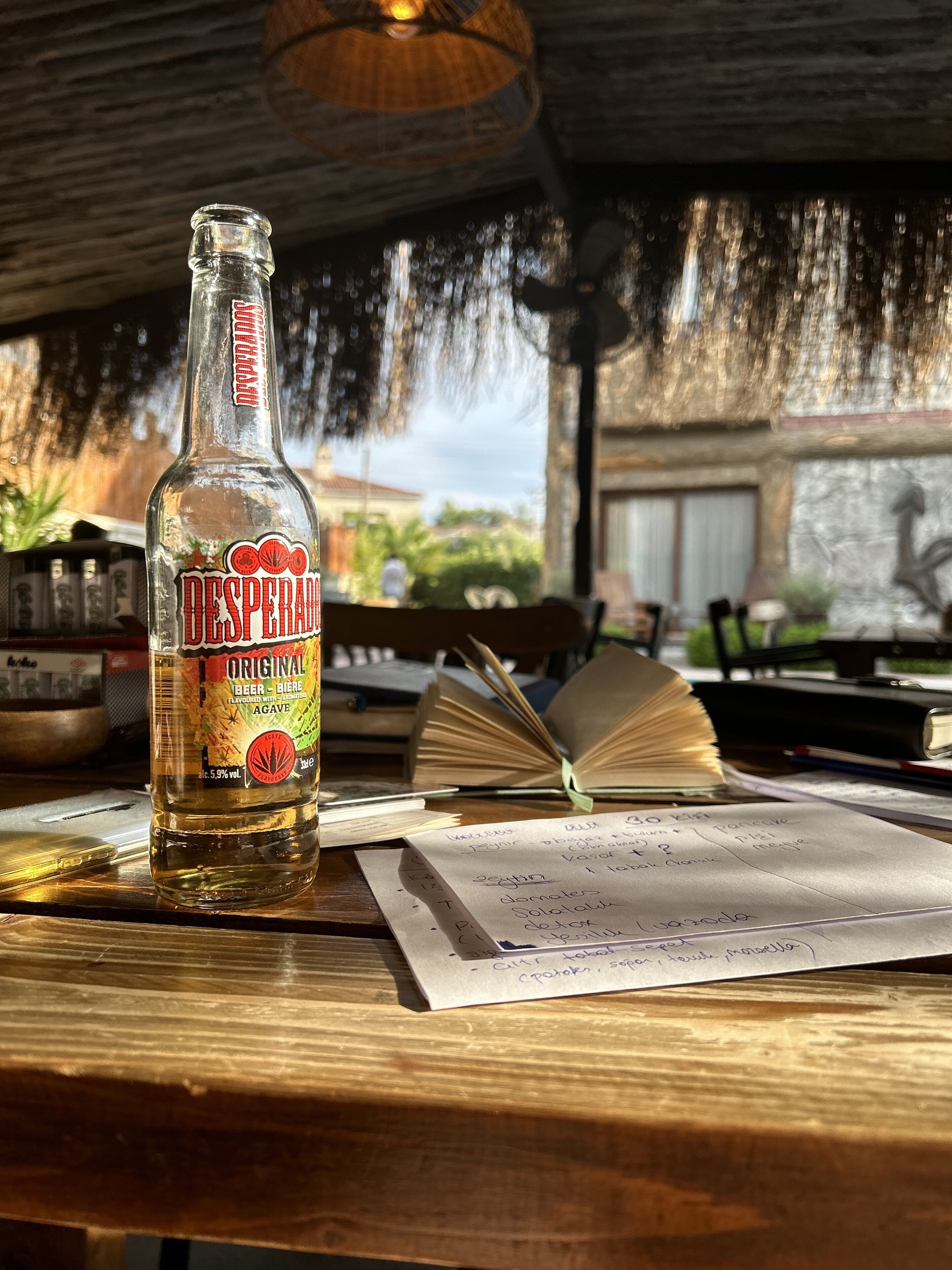 Una botella de cerveza Desperado Original sobre una mesa de madera con un libro abierto y papeles.