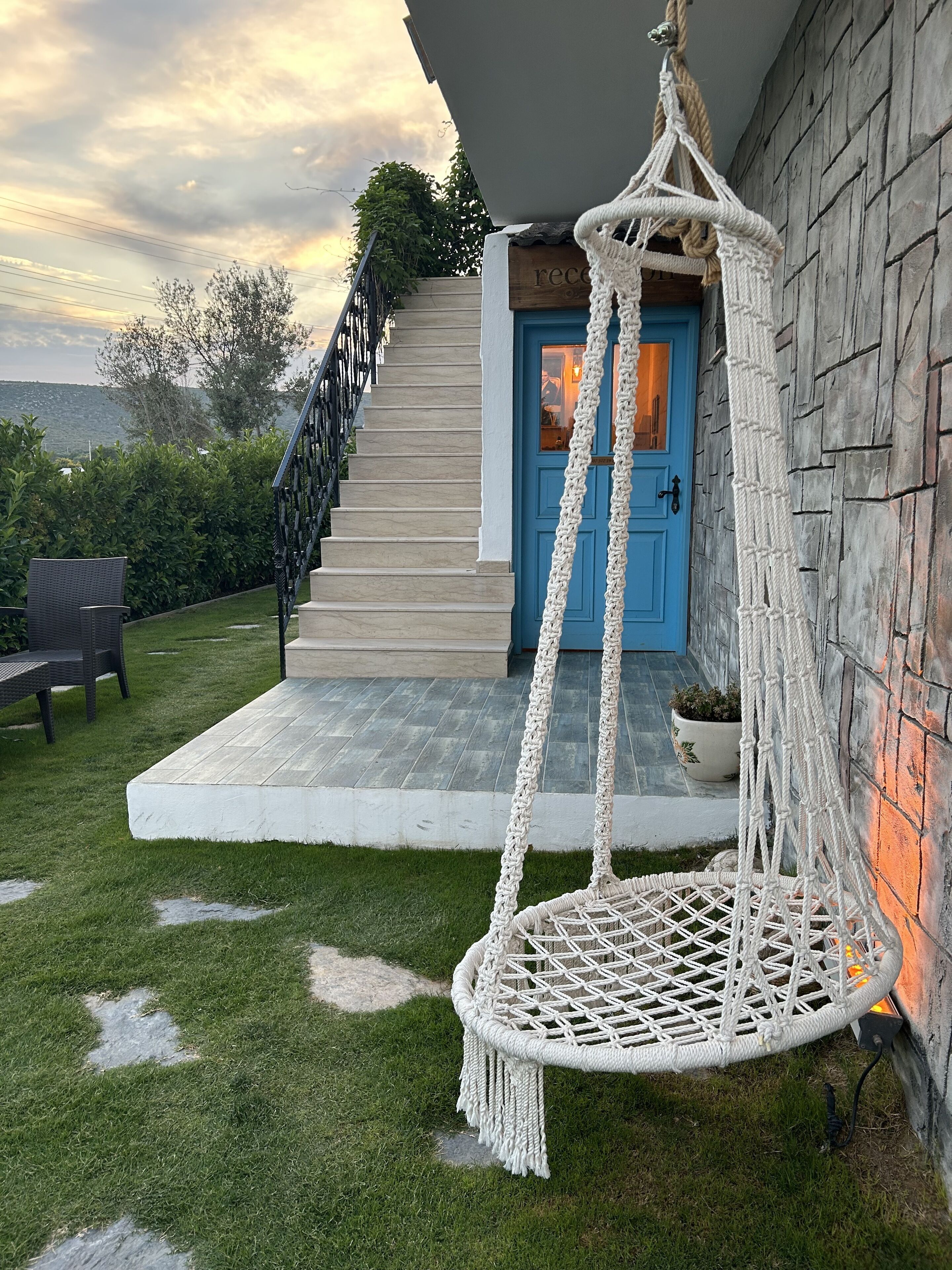 A house with a blue door, a macrame swing chair, and a staircase leading to the entrance.