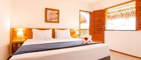 A hotel room with a large bed, wooden headboard, two bedside lamps, a framed picture on the wall, and a window with wooden shutters.