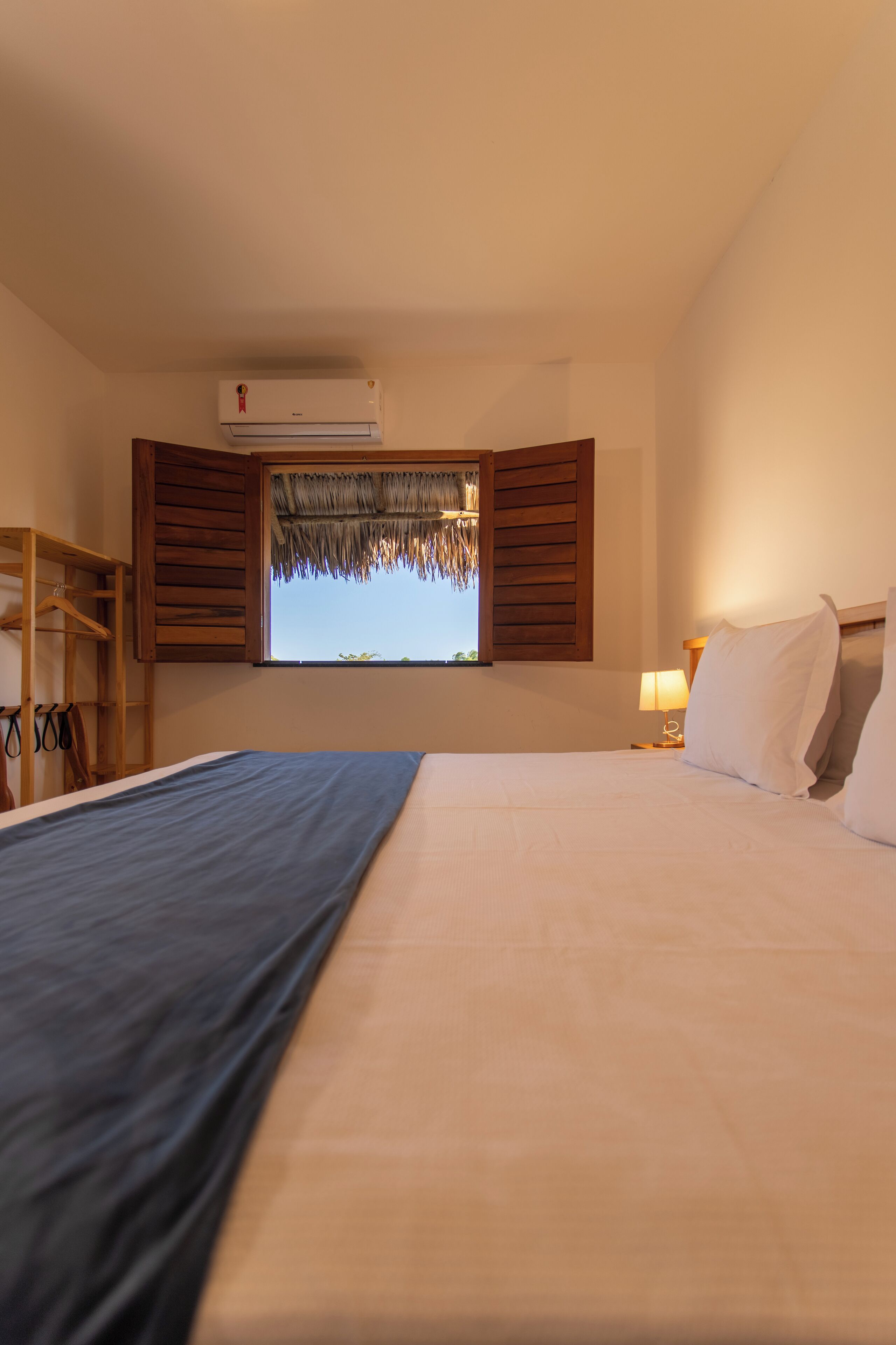 A bedroom with a bed, a window with wooden shutters, a hanging wardrobe, and a ceiling fan.