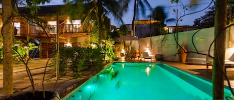 A swimming pool with a tiled deck, surrounded by potted plants and palm trees.