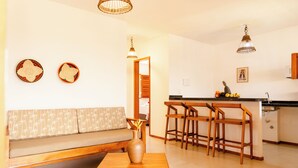 Una sala de estar moderna con un sofá de madera, una pequeña mesa con un jarrón y una cocina con taburetes de madera y una encimera negra.