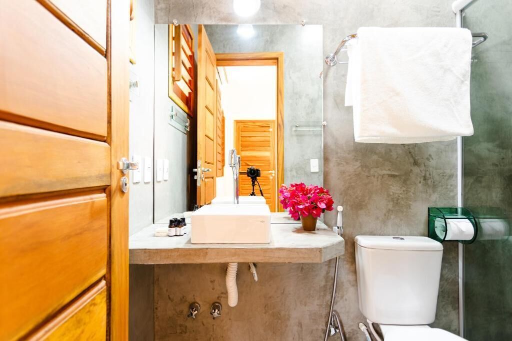 Un baño con puerta de madera, un lavabo blanco, un espejo, un inodoro y un dispensador de jabón de vidrio.