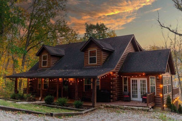Une cabane en rondins avec un porche, un espace couvert agrémenté de guirlandes lumineuses et un chemin en pierre.