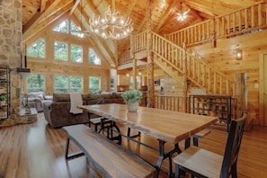 Une cabane en bois spacieuse, dotée d’un coin repas, d’un escalier et de grandes fenêtres.