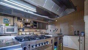 Uma cozinha comercial equipada com eletrodomésticos de aço inoxidável, incluindo fogão, forno e micro-ondas.