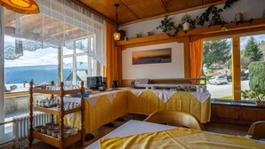 Quarto acolhedor com teto de madeira, uma janela grande com vista para o exterior, uma mesa com toalha amarela e um radiador.