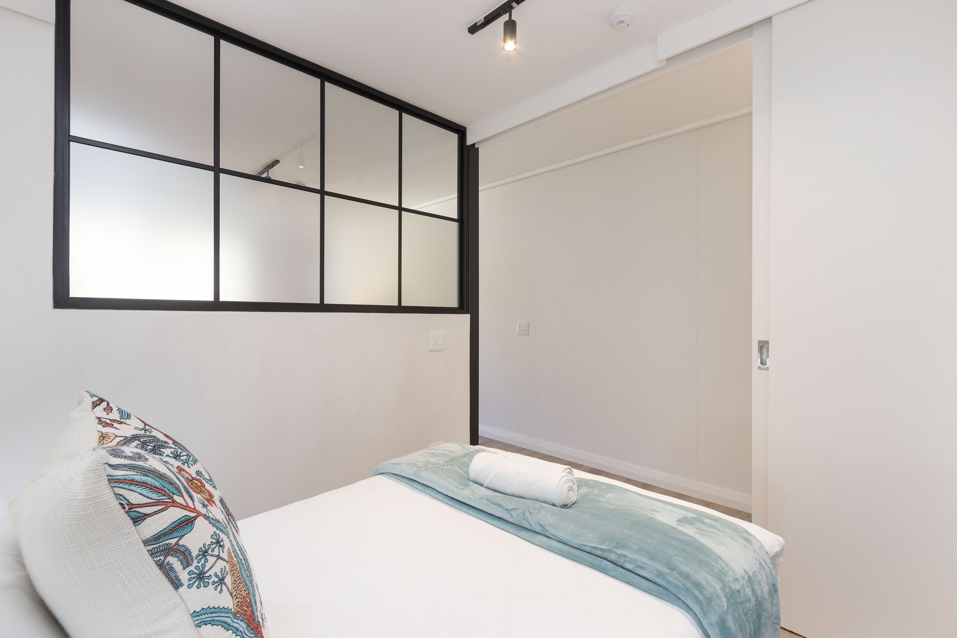 A bedroom with a bed, a pillow, a wall-mounted mirror, and a door.
