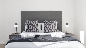 A modern bedroom with a large bed, grey headboard, patterned pillows, bedside lamps, and a dark throw blanket. - The Cedar Unit 105 (Cape Town)