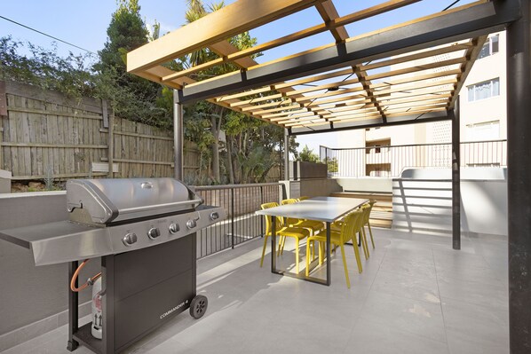 An outdoor patio with a grill, yellow chairs, and a pergola.