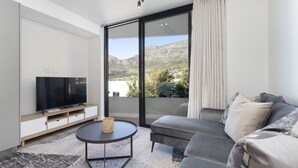 A modern living room with a flat-screen TV, a round coffee table, and a grey sofa. - The Cedar Unit 105 (Cape Town)