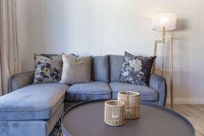 A modern living room with a grey sectional sofa, two woven side tables, and a floor lamp.