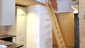 Eine Küche mit weißen Schränken, einer schwarzen Arbeitsplatte und einer Holzleiter zu einem Erkerraum.