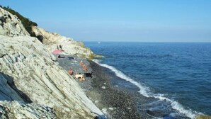 Ein felsiger Strand mit Menschen und einem Hund, strahlend blauer Himmel und ruhiges Meer.