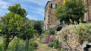 A stone building with a rustic appearance, featuring a small archway and a garden with various plants and a stone wall. - Casa Ferrando by Interhome (Torrazza)