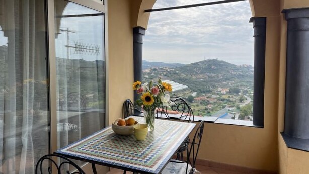 A balcony with a table, chairs, a vase with flowers, and a view of a landscape. - Casa Ferrando by Interhome (Torrazza)