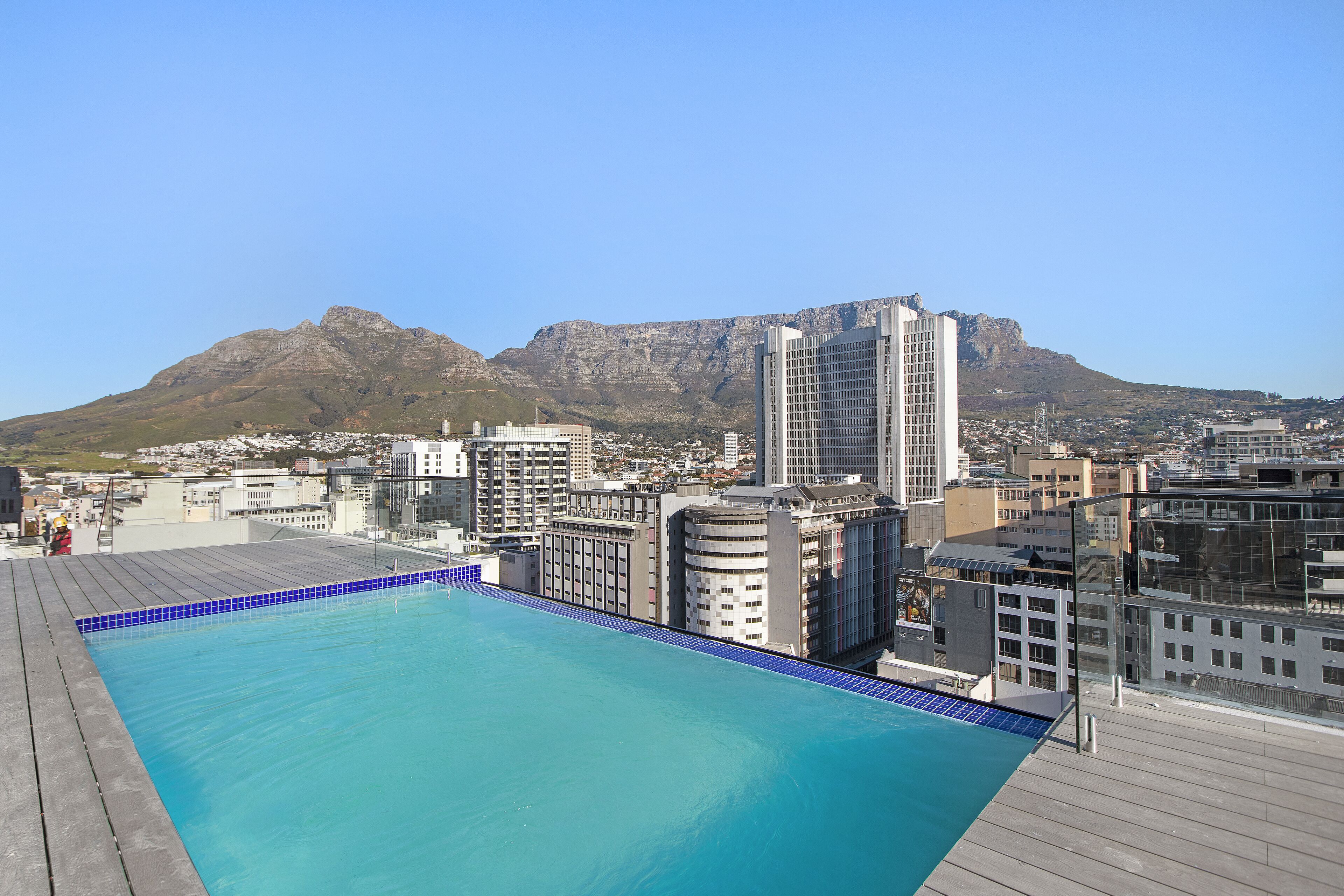 A rooftop pool with a cityscape and mountains in the background.