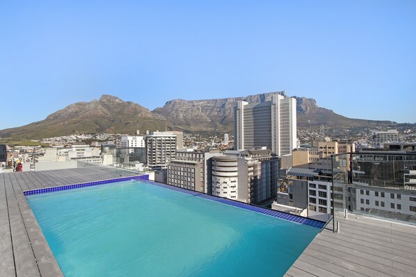 A rooftop pool with a cityscape and mountains in the background.