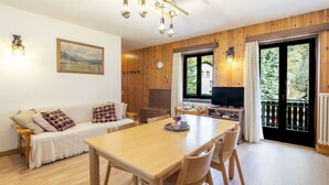 A cozy living room with a wooden dining table, a sofa with patterned cushions, a painting on the wall, and a television in the corner. - Isola di Madesimo Apartments by Interhome (Madesimo)