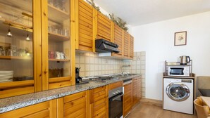 A compact kitchen with wooden cabinets, a built-in oven, a microwave, and a washing machine. - Isola di Madesimo Apartments by Interhome (Madesimo)