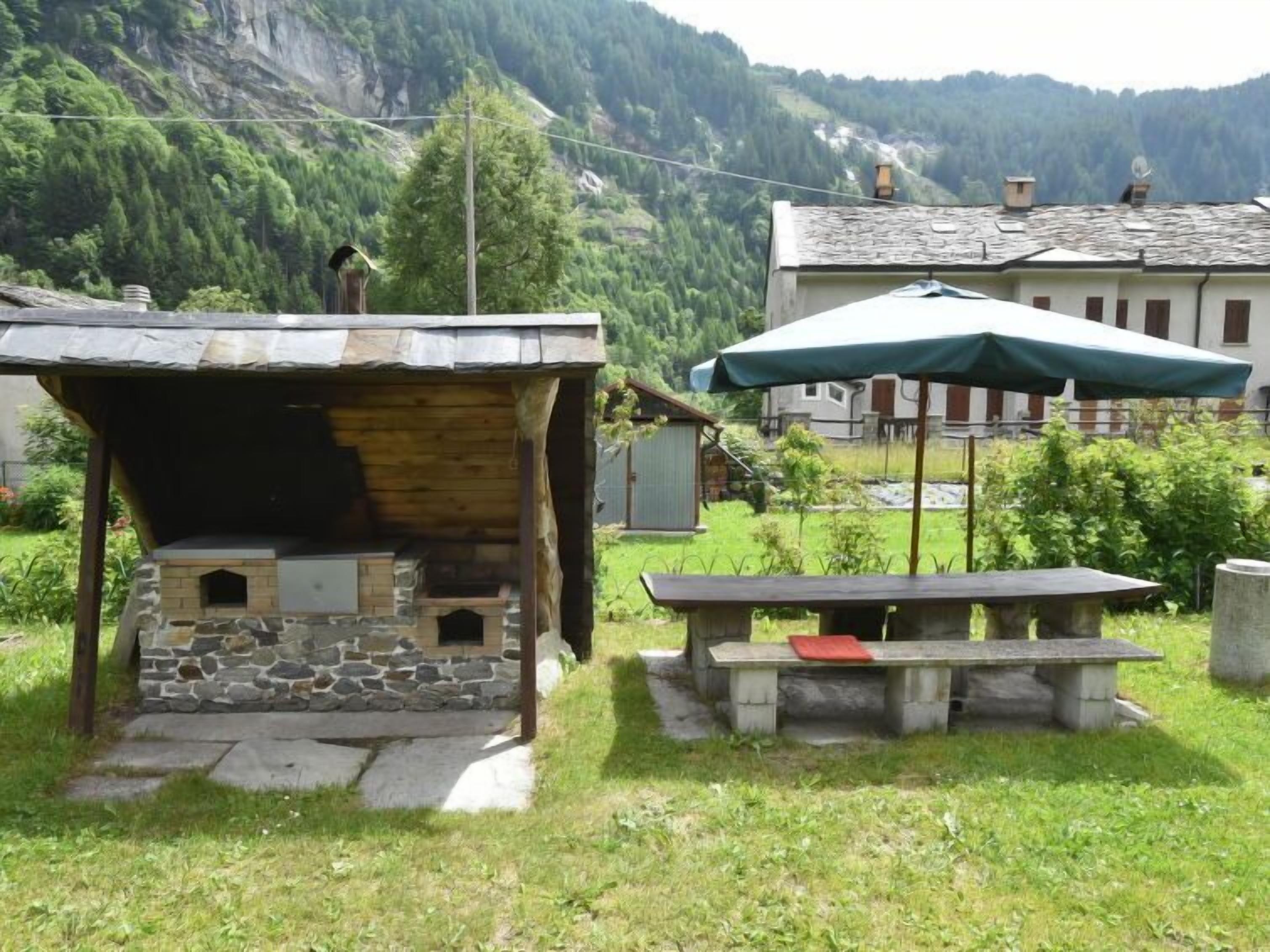 Un'area cucina esterna rustica con forno in pietra, tavolo da picnic e ombrello verde.