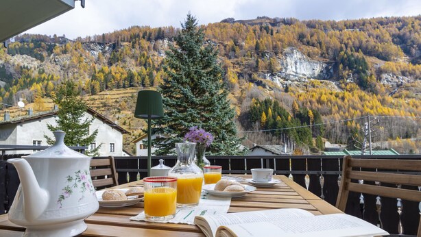 A wooden table with a teapot, a book, a glass of orange juice, and a plate of pastries. - Isola di Madesimo Apartments by Interhome (Madesimo)