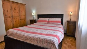 Une chambre à coucher avec un lit, une armoire en bois, deux tables de chevet avec des lampes et un plancher en bois.