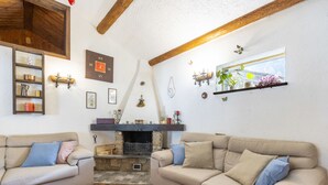 Un salon chaleureux avec deux canapés beige, une cheminée en pierre, des poutres en bois et une décoration rustique.