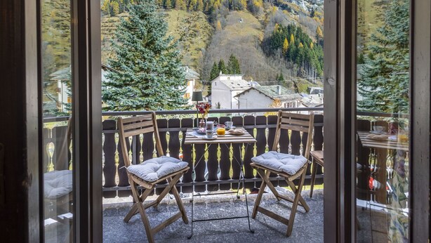 Un balcon avec deux chaises en bois et une table, donnant sur un paysage montagneux aux couleurs automnales.