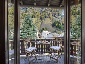 Un balcon avec deux chaises en bois et une table, donnant sur un paysage montagneux aux couleurs automnales.