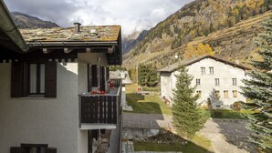 Vue d’un bâtiment avec balcon, pris depuis le flanc d’une montagne, avec un ciel dégagé et des arbres aux couleurs automnales en arrière-plan.