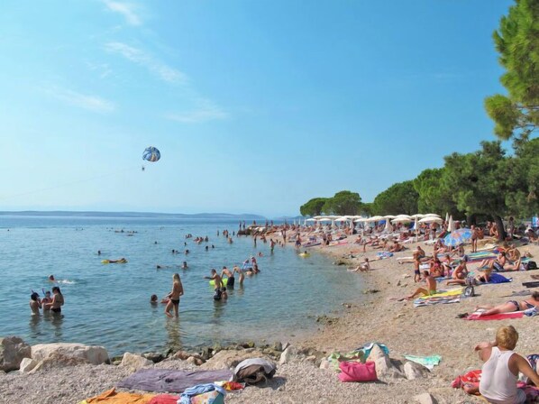 Une plage bondée où l’on voit des gens se baigner et bronzer, des parasols et des chaises de plage.