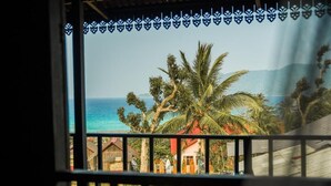 A view from a window with a decorative border, overlooking a coastal area with palm trees and buildings. - Harrera Perhentian Long Beach (Pulau Perhentian Kecil)