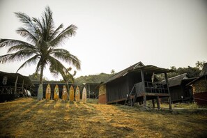 A rural setting with a palm tree, wooden buildings, and surfboards with letters. - Harrera Perhentian Long Beach (Pulau Perhentian Kecil)