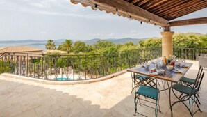 Un patio techado al aire libre con una mesa lista para comer, una piscina y vistas del paisaje.
