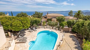 Una piscina con solárium de piedra, rodeada de sillones de descanso y vistas al mar.