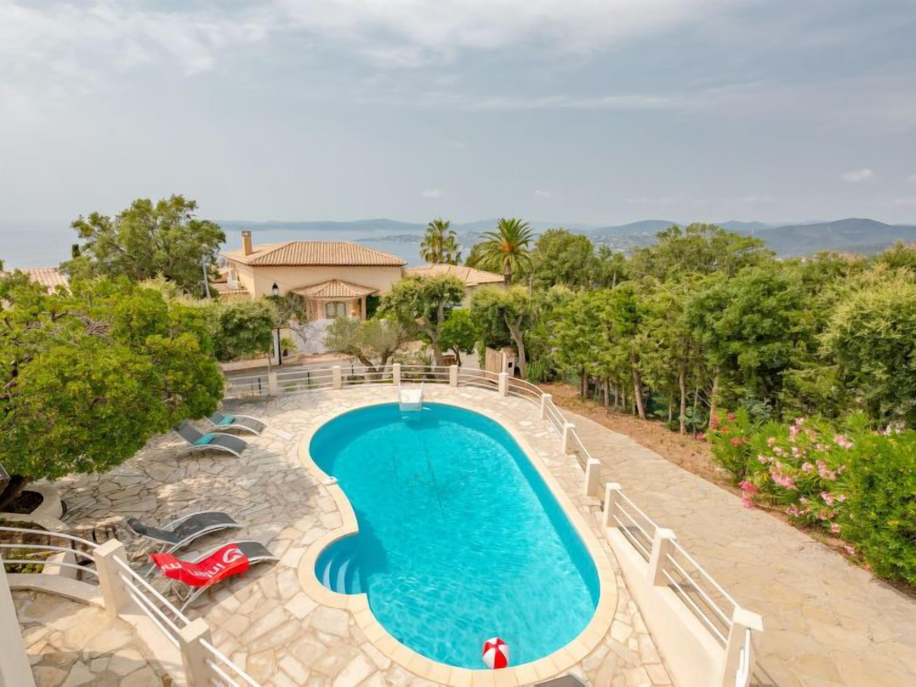 A swimming pool with a stone deck, surrounded by greenery and a view of mountains.
