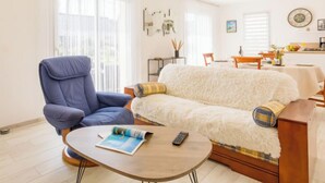 Een woonkamer met een blauwe fauteuil, een witte bank, een houten salontafel en een eethoek op de achtergrond.